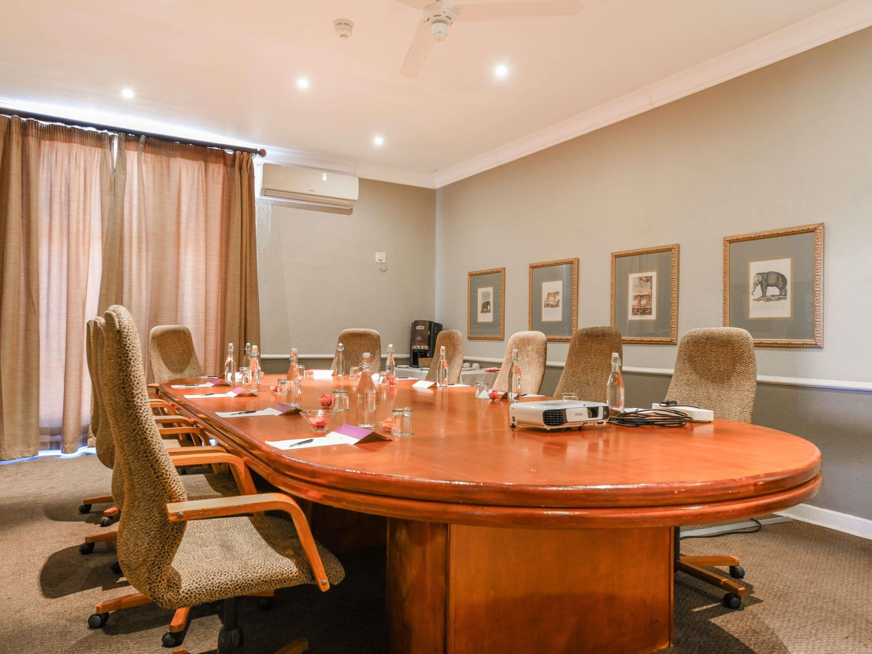 A conference room with a large oval table, six chairs, a projector, and framed pictures on the wall.