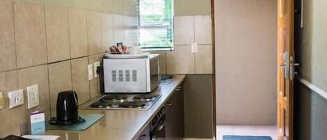 A compact kitchen with a microwave, stove, and coffee maker. A door leads to a hallway.