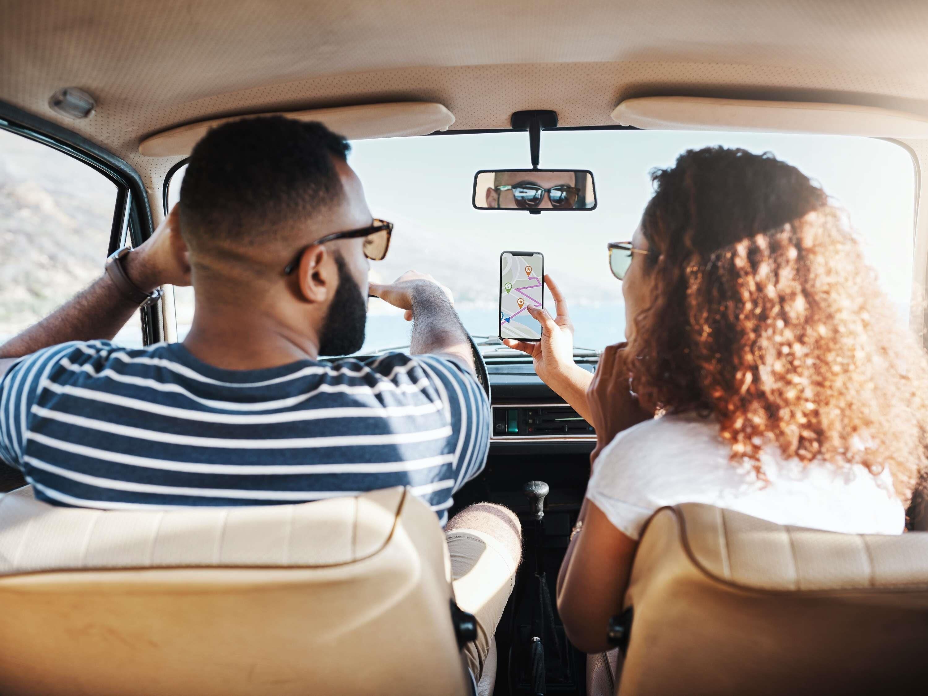 A car interior with two passengers, one holding a smartphone.