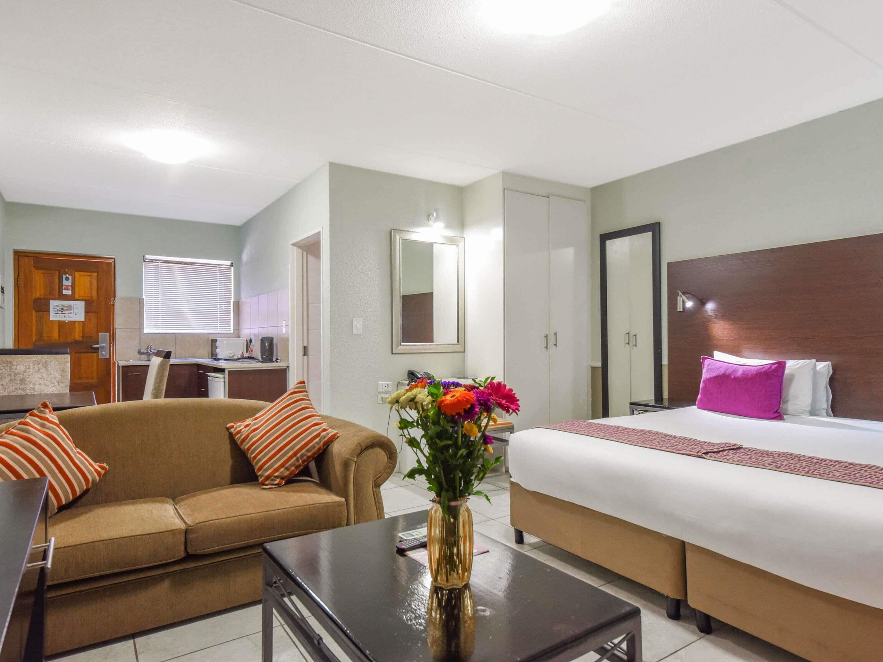 Quarto de hotel com cama, sofá, mesa de centro, espelho e janela.