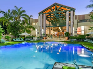 A hotel with a pool, outdoor seating, and a covered area with stairs leading to the entrance. - Mercure Nelspruit Hotel (Mbombela)