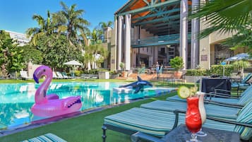 Relax by the pool with a drink in hand, surrounded by palm trees and a lawn.