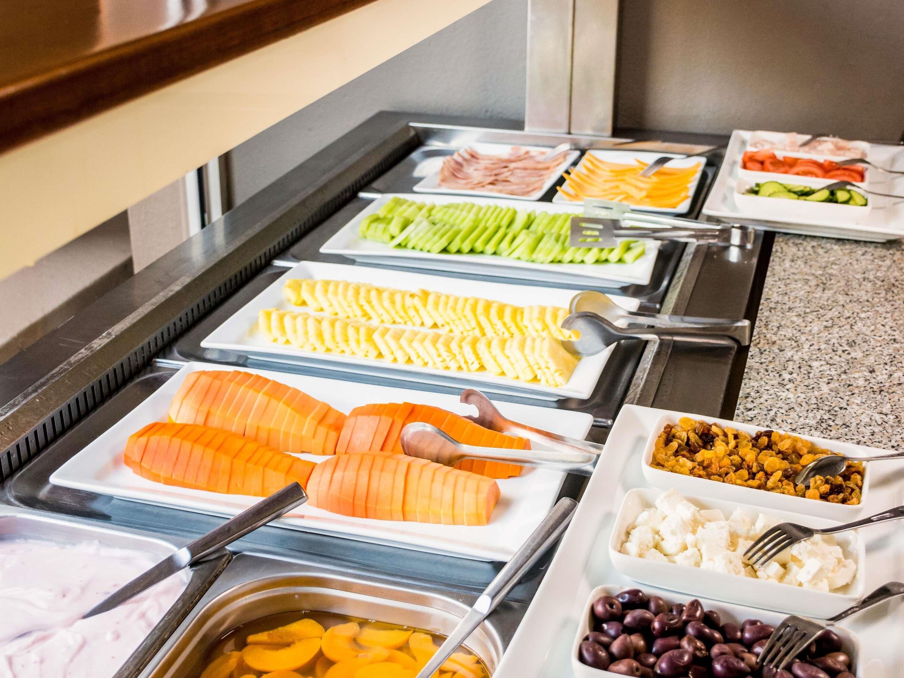 A buffet with various food items including sliced salmon, cheese, vegetables, and fruits.