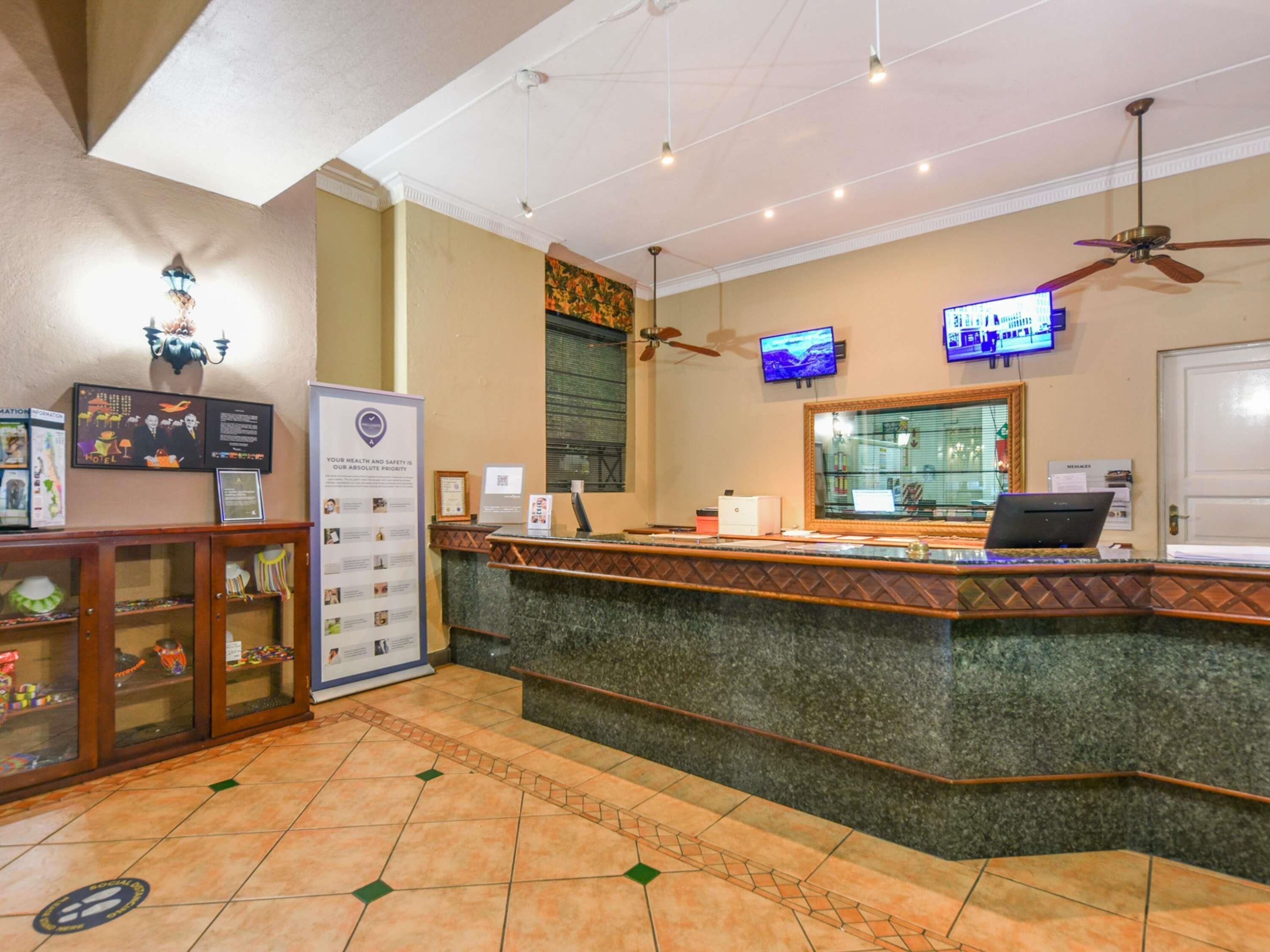 A hotel reception area with a marble counter, a reception desk, a television screen, a ceiling fan, and a wall-mounted sign.