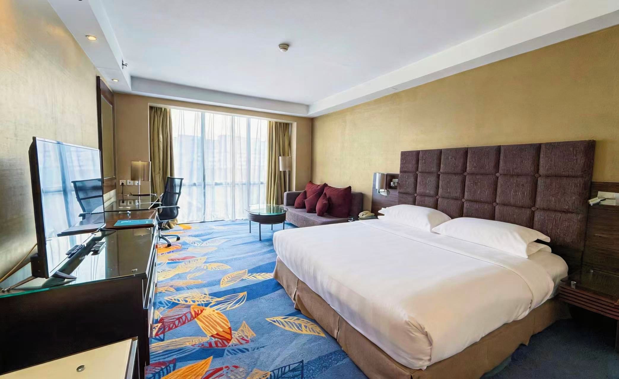 A hotel room with a large bed, a desk with a laptop, a chair, and a TV.