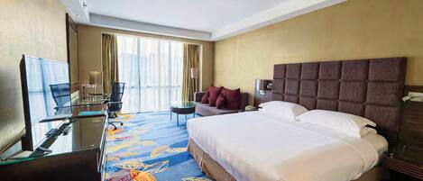 A hotel room with a large bed, a desk with a laptop, a chair, and a TV.
