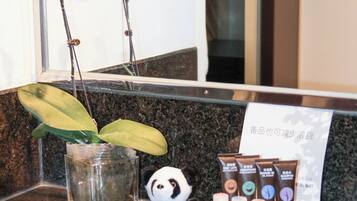 A bathroom counter with a glass vase containing orchids, a panda figurine, and a set of toiletries.