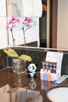A bathroom counter with a glass vase containing orchids, a panda figurine, and a set of toiletries.