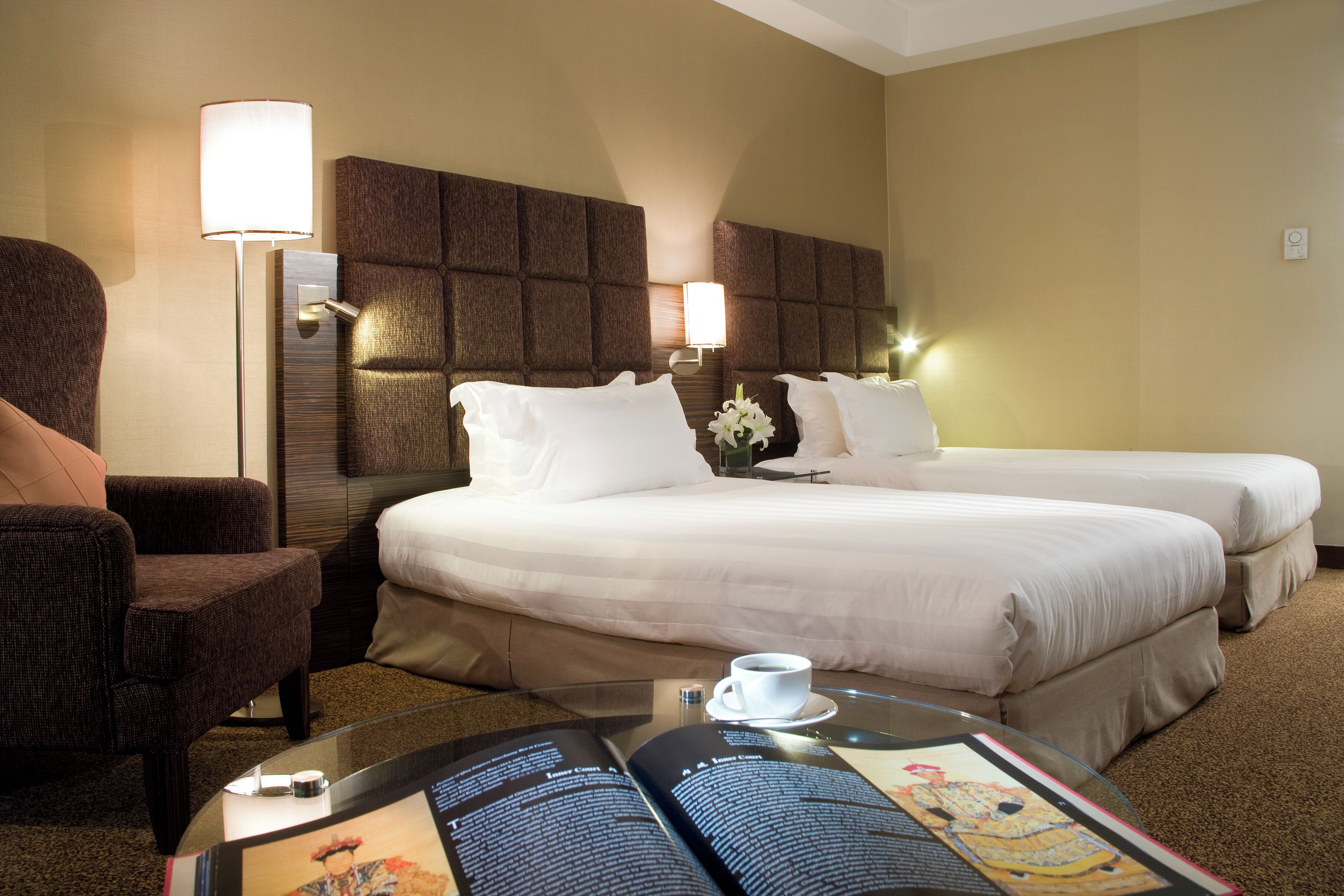 Habitación de hotel con dos camas, un sofá, una lámpara y una mesa de centro con una revista.