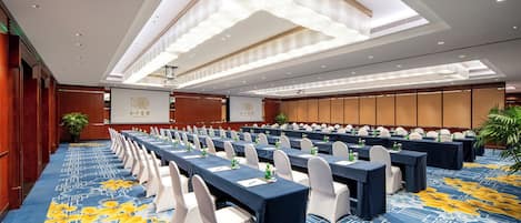 A conference room with rows of tables, chairs, and a large screen.
