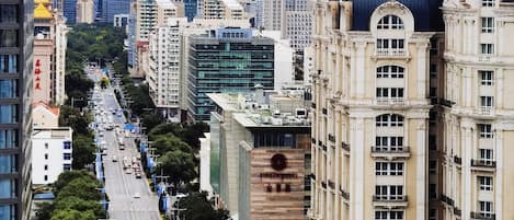 Un paysage urbain avec des gratte-ciel modernes, un bâtiment historique surmonté d’un dôme et une rue animée où circulent des voitures.