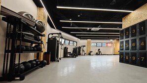 Un gimnasio con equipo de levantamiento de pesas, máquinas de ejercicio y una pared con taquillas numeradas.