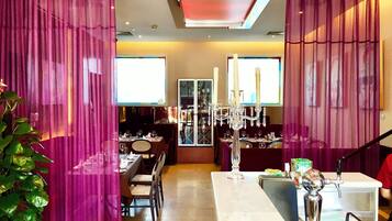 A dining area with a long table, chairs, a chandelier, and a bar area with a counter and stools.