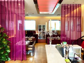 A dining area with a long table, chairs, a chandelier, and a bar area with a counter and stools.