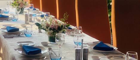 Mesa de comedor dispuesta con servilletas azules, vasos transparentes y cubertería, con vista a la ciudad a través de amplias ventanas.