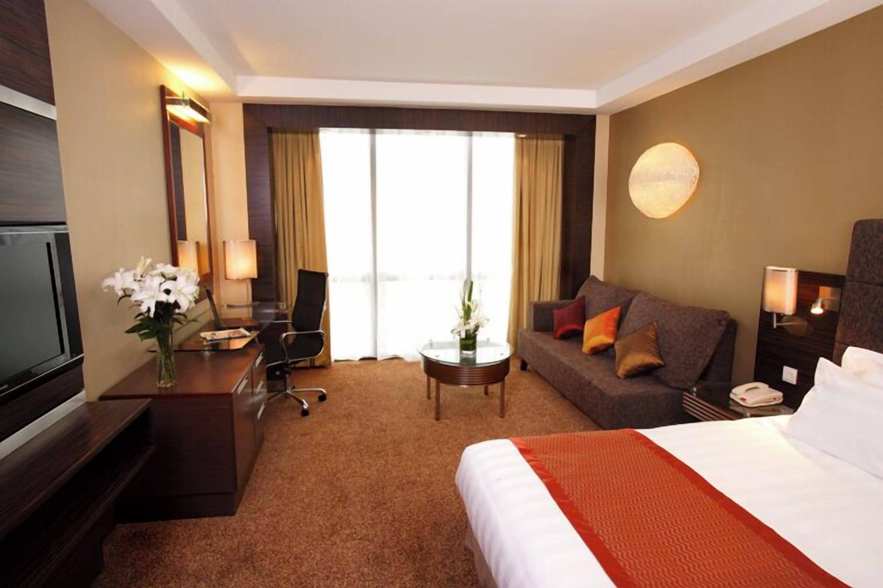 A hotel room with a bed, a desk, a sofa, a TV, and a large window.