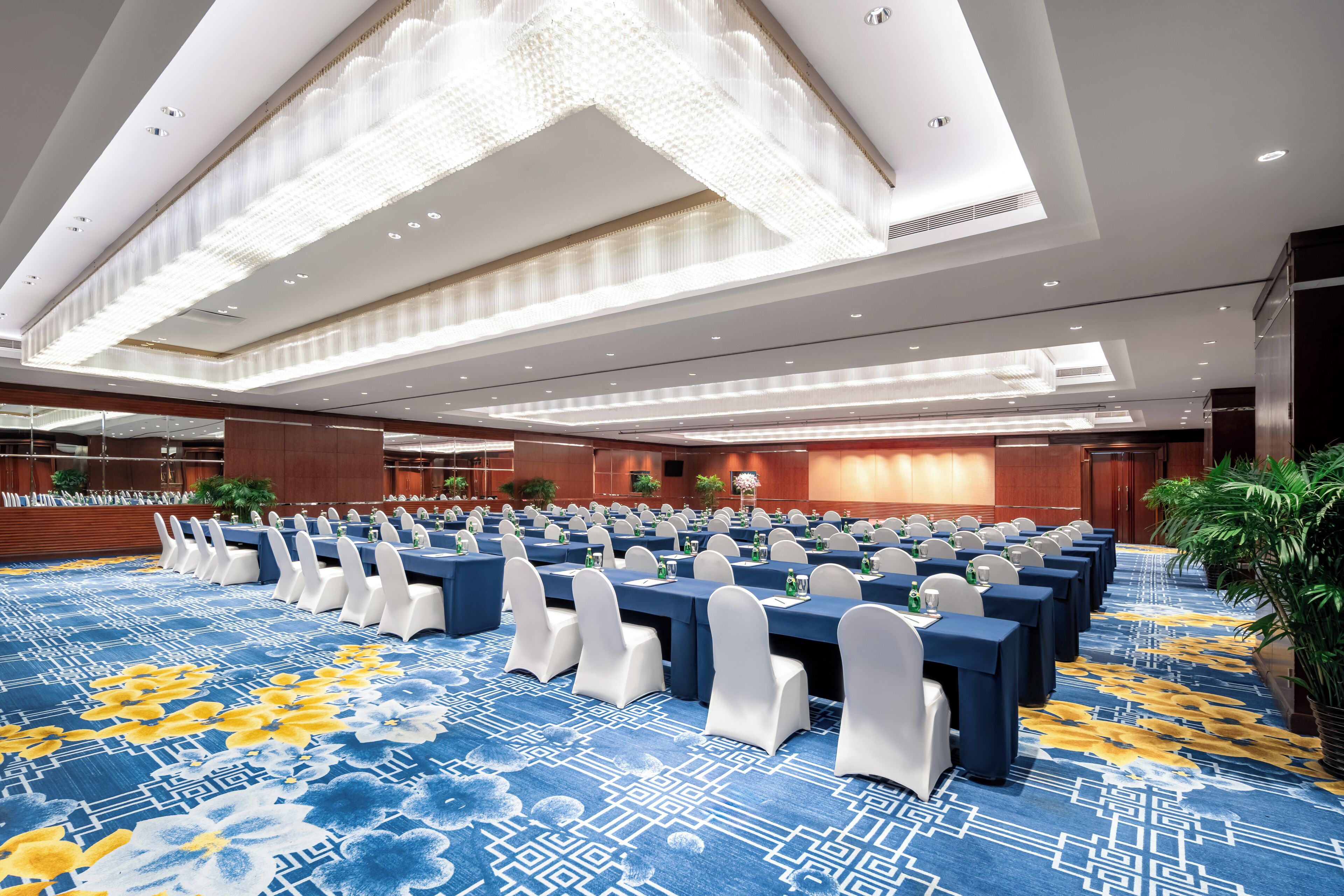 A conference room with rows of tables, white chairs, and a patterned carpet.
