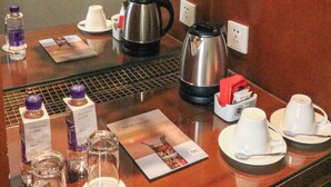 Zona de recepción de un hotel con una estación de café, botellas de agua y una figurita de panda en un estante.