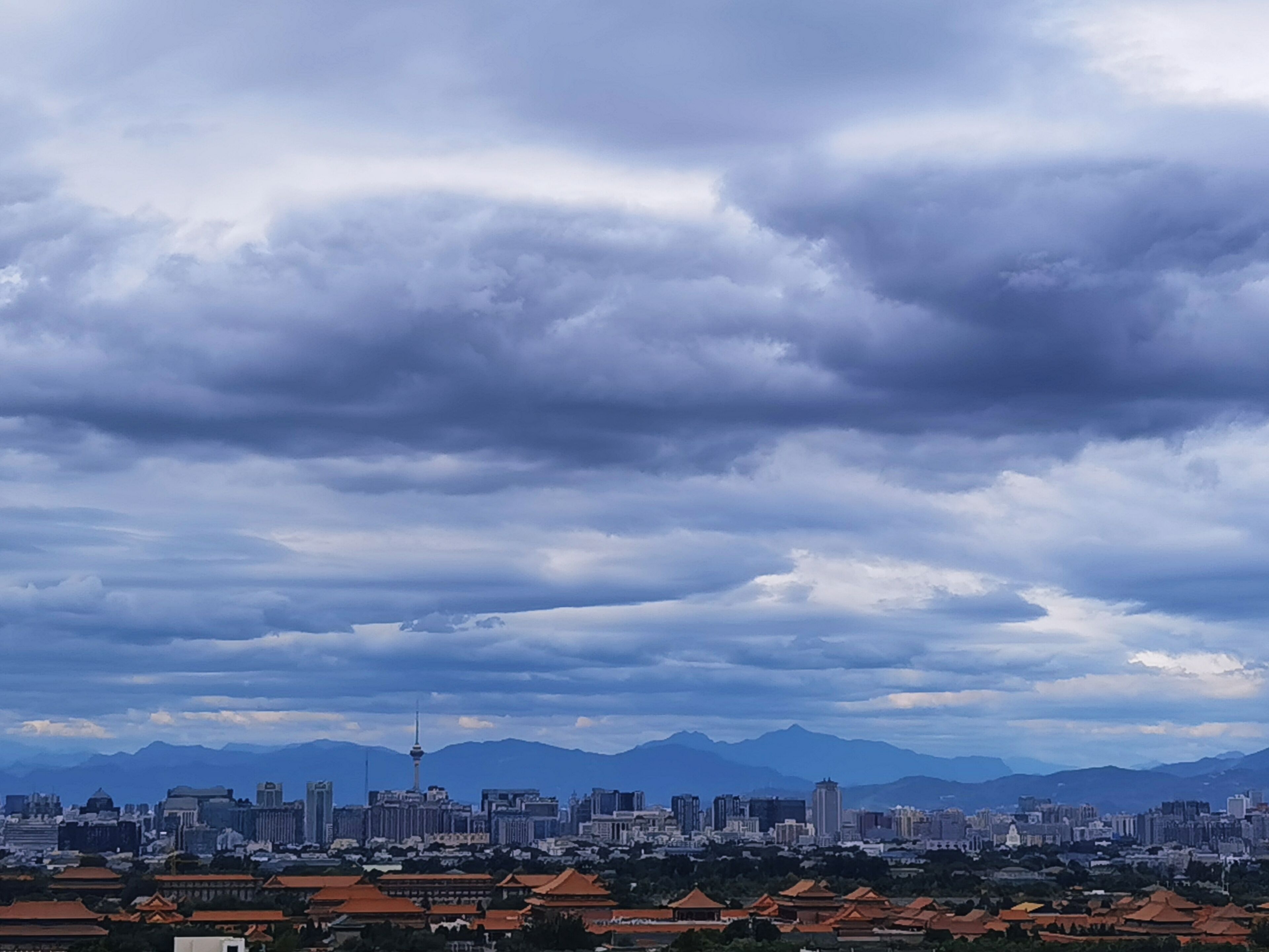 Un paisaje urbano que combina arquitectura tradicional y moderna, con una torre destacada y montañas al fondo bajo un cielo nublado.