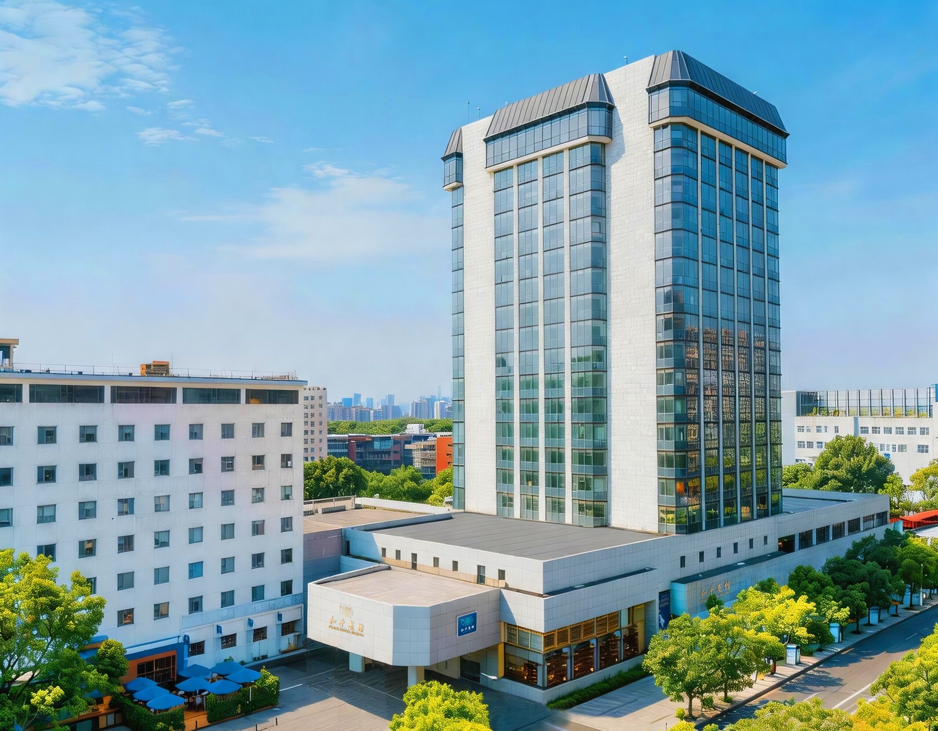 A modern hotel with a prominent glass facade, a flat roof, and a courtyard with outdoor seating.