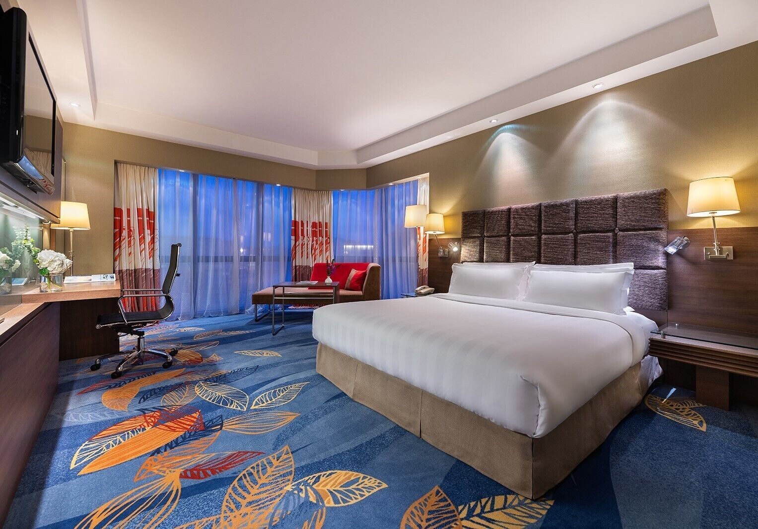 A hotel room with a large bed, a desk with a chair, a small table with a chair, and a TV.