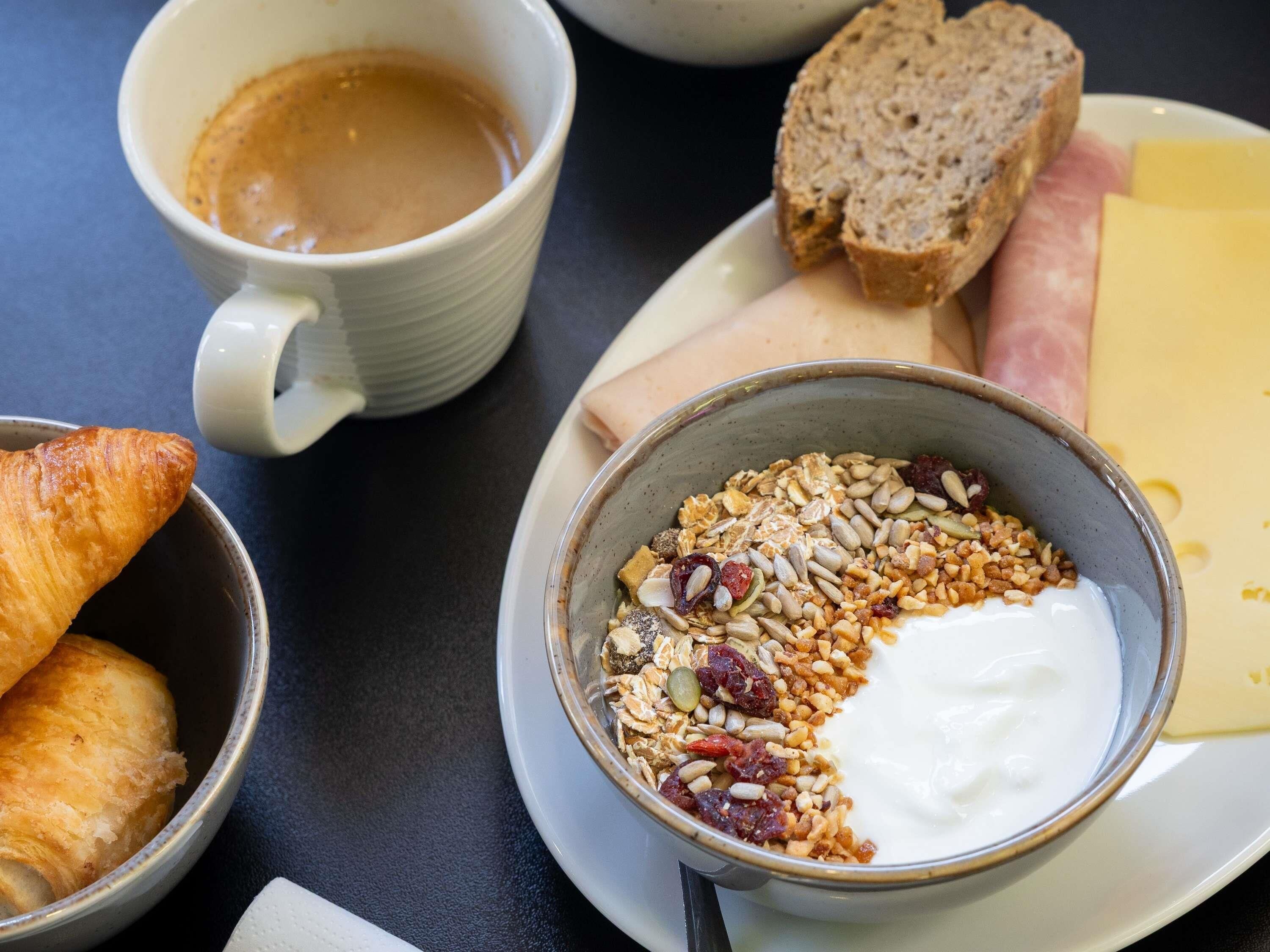A breakfast setting with croissants, a bowl of yogurt with granola, cheese, ham, and bread.