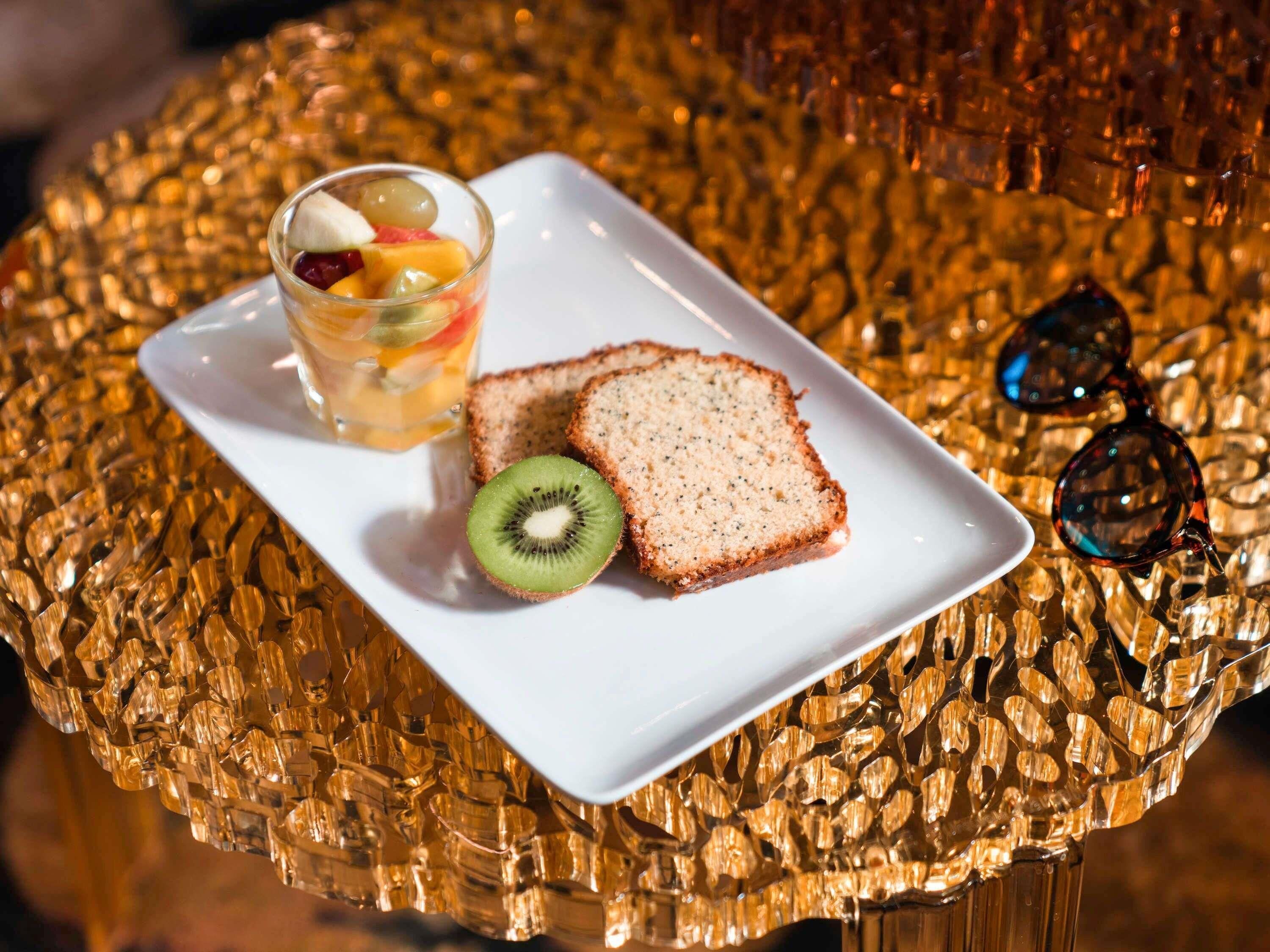 Une tranche de pain sur une assiette blanche, un verre de jus de fruits et un kiwi sur une surface texturée.
