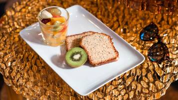 Una rebanada de pan sobre un plato blanco, un vaso de jugo de fruta y un kiwi sobre una superficie rugosa.