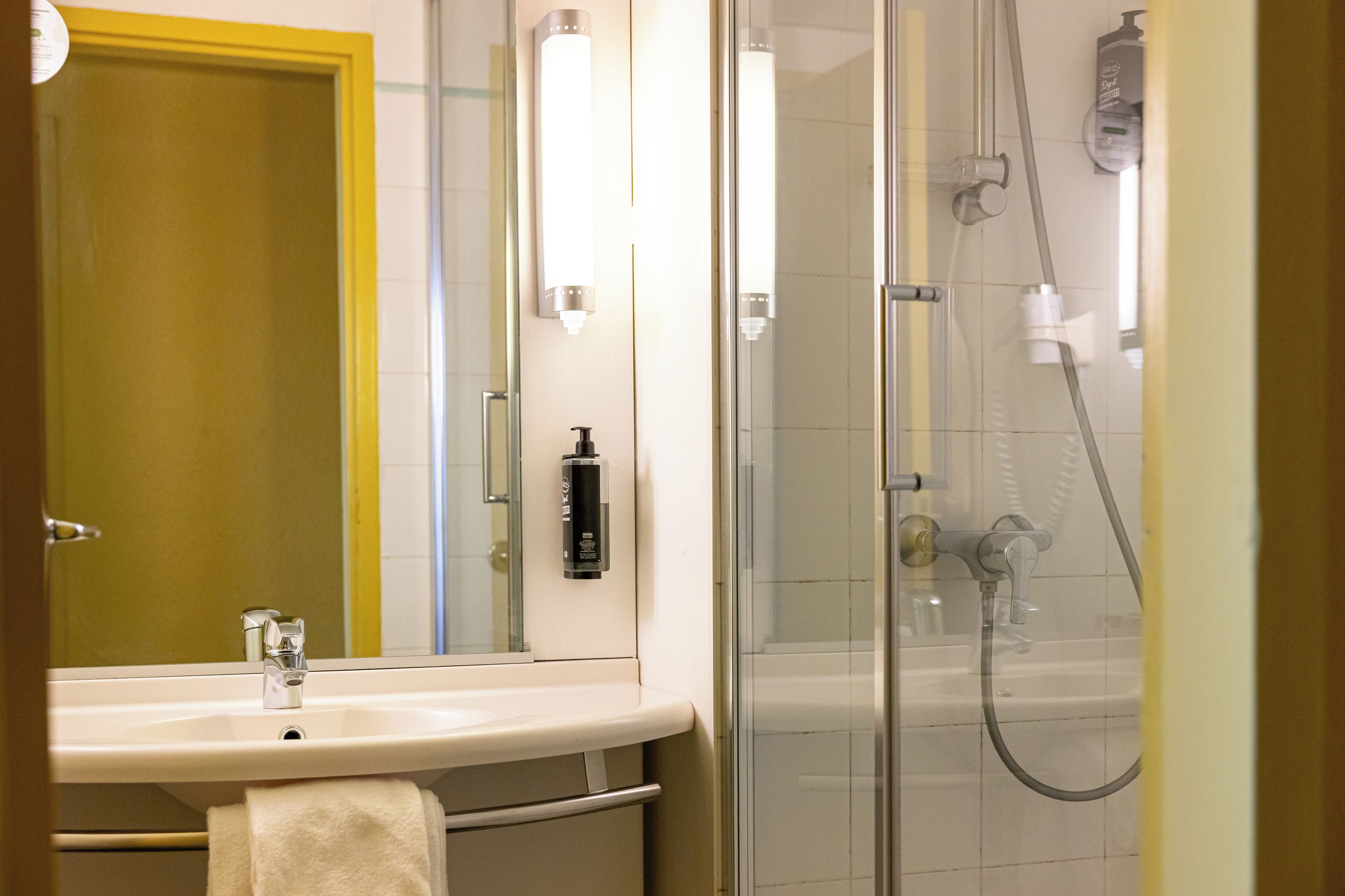 A bathroom with a sink, mirror, shower, and towel rack.