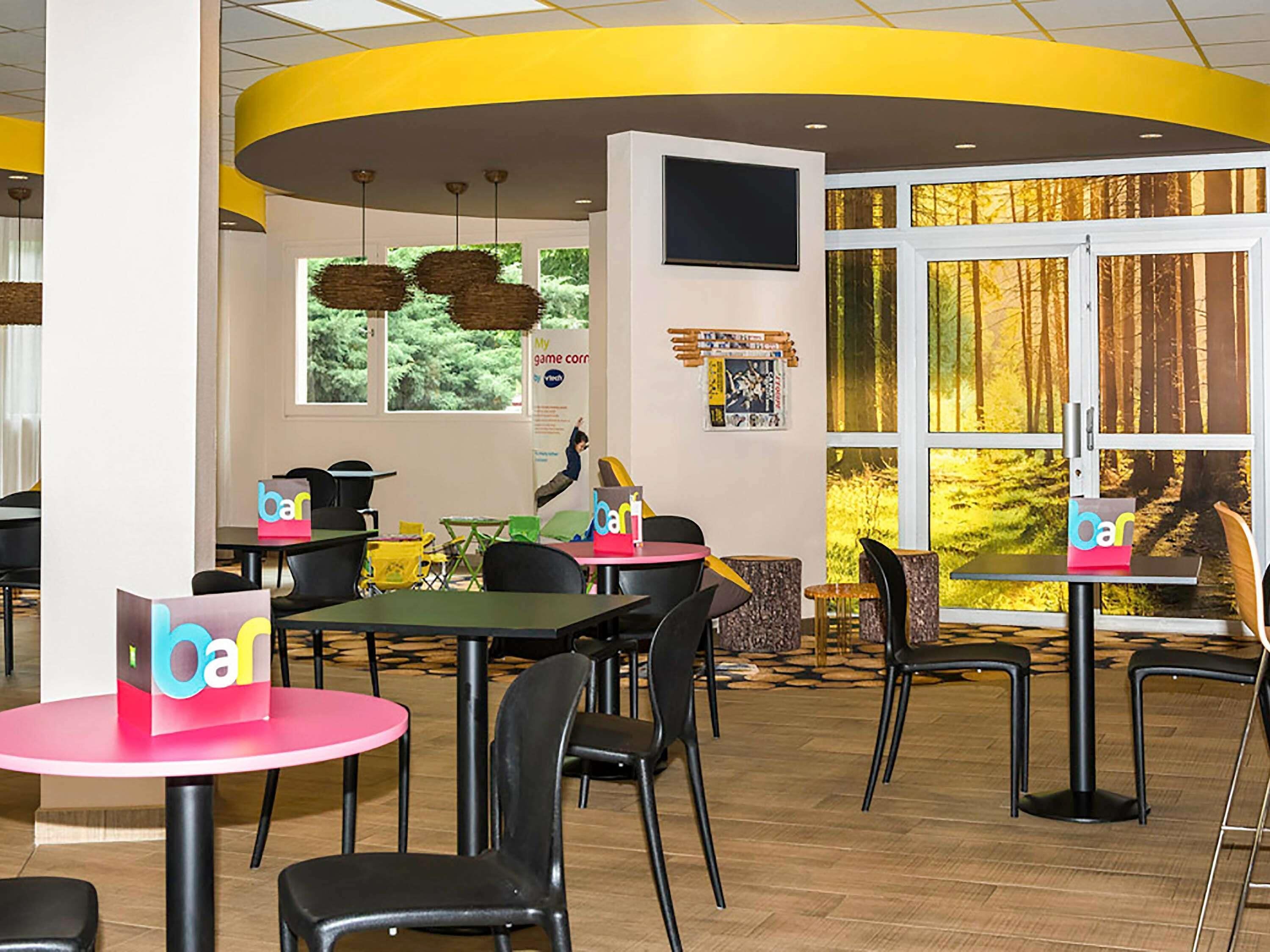 A modern dining area with round tables, black chairs, and a yellow accent wall.