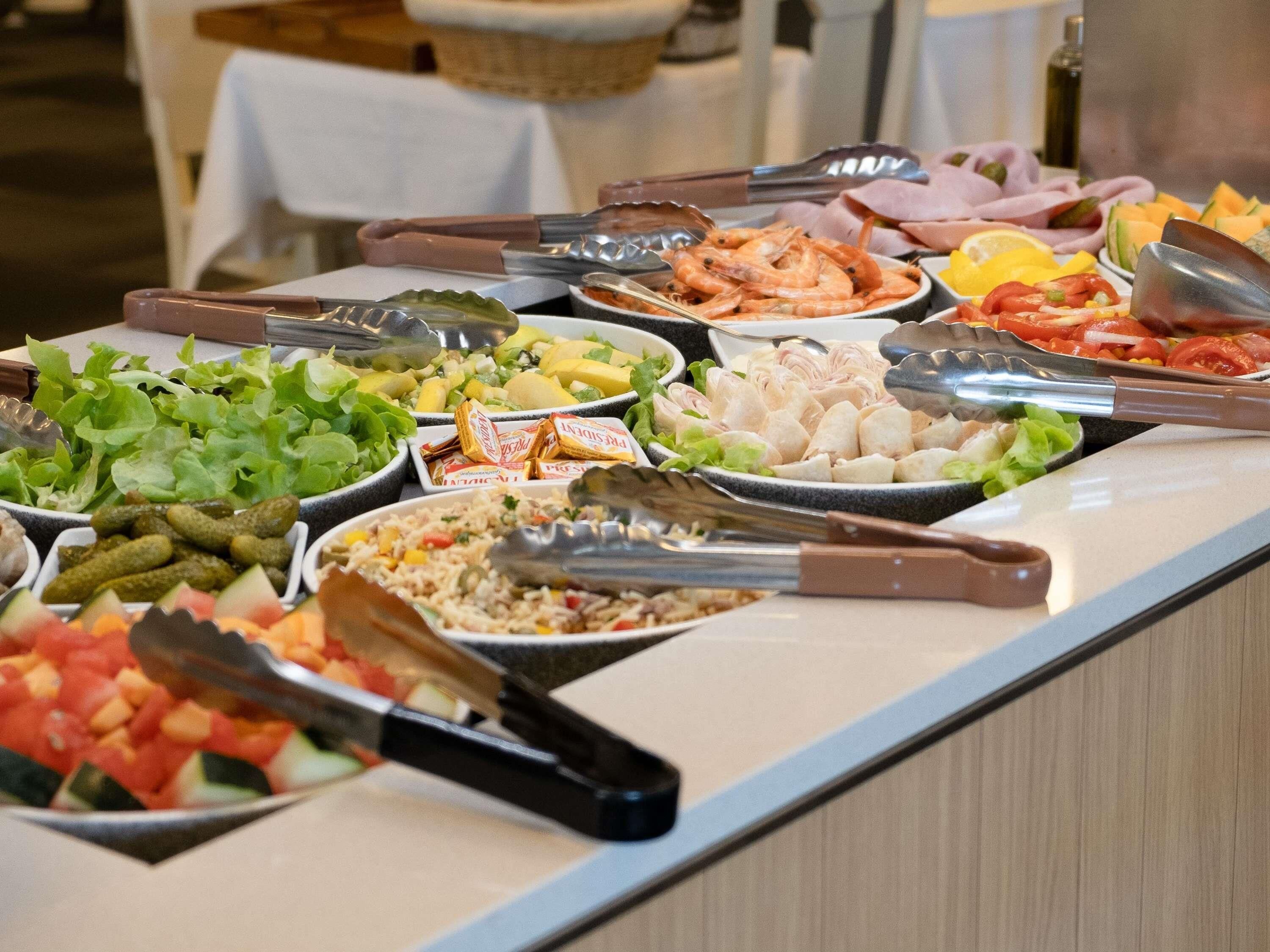 Un bufé con diversas opciones de comida, entre ellas ensaladas, frutas y carnes.