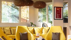 Una sala de estar moderna con sofás y sillones amarillos, una mesa de centro redonda y ventanas amplias con vistas a árboles.