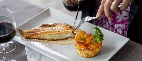 A dining table with a white plate containing a fish fillet and a baked item, possibly a muffin or tart, with a garnish.