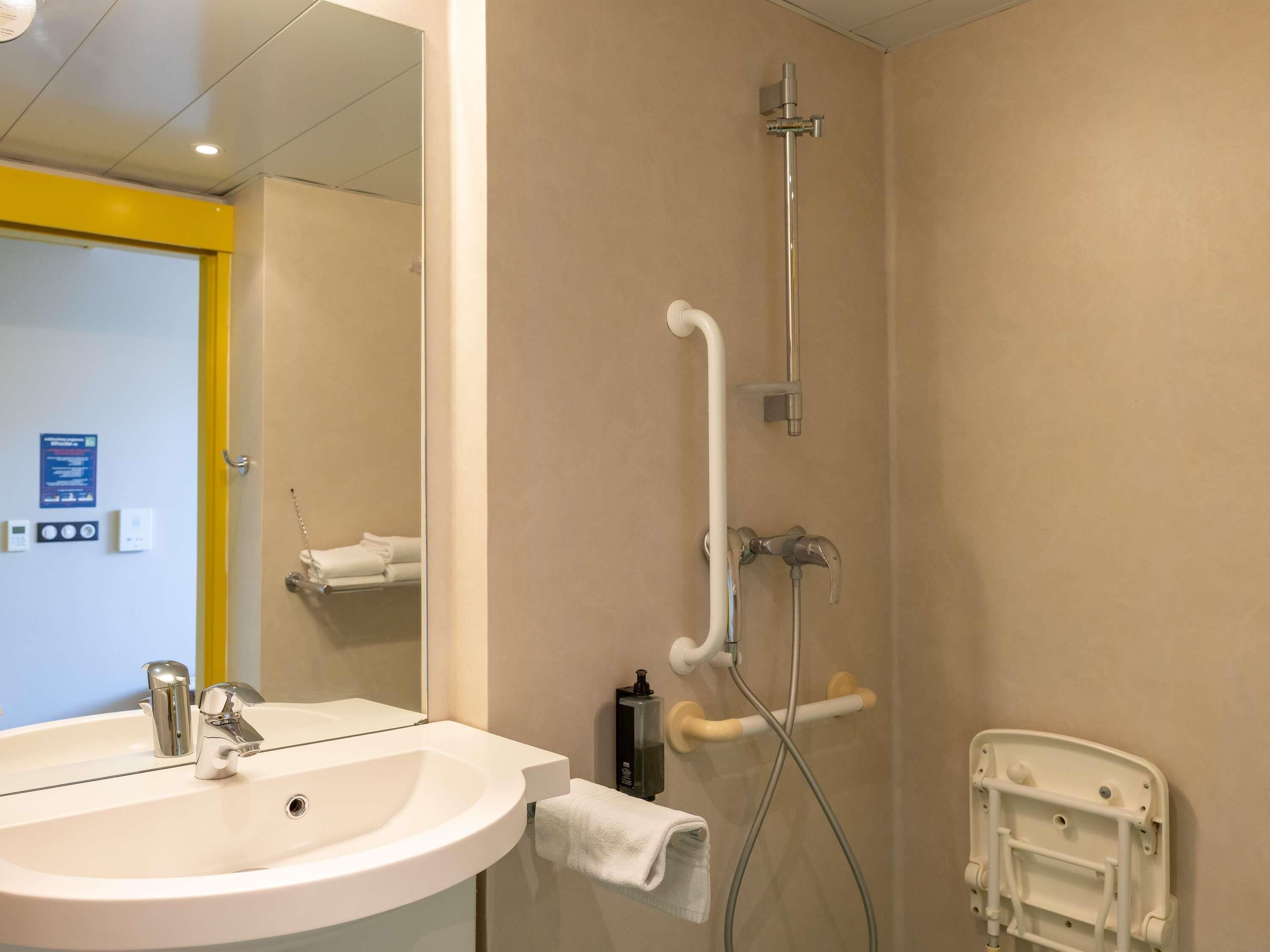 A bathroom with a sink, mirror, shower, and a white chair.