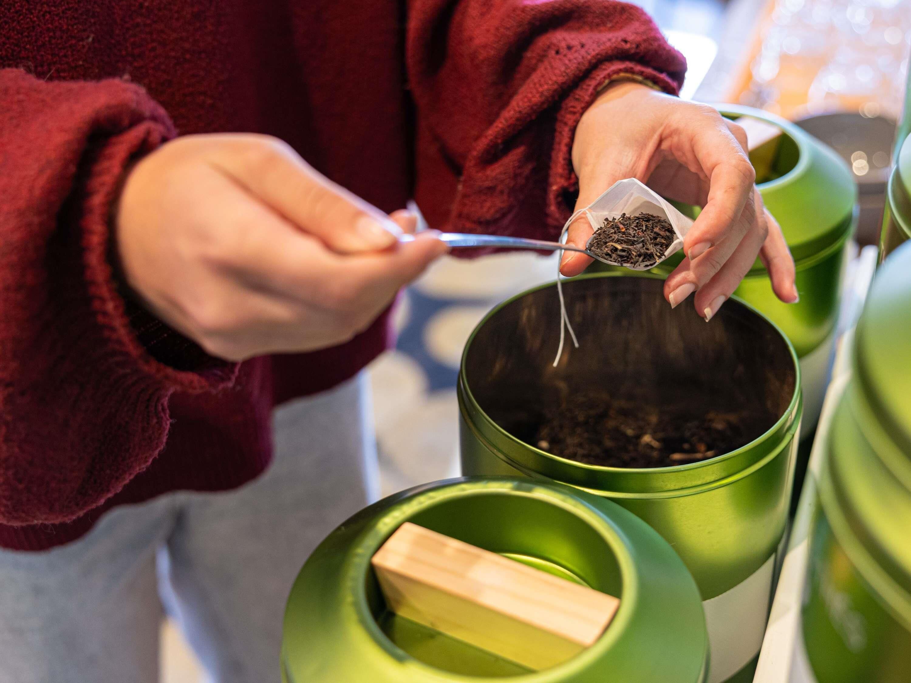 Una persona sosteniendo un pequeño paquete de hojas de té, a punto de agregarlas a un recipiente verde.