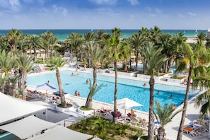 A resort pool area with multiple swimming pools, surrounded by palm trees and lounge chairs.