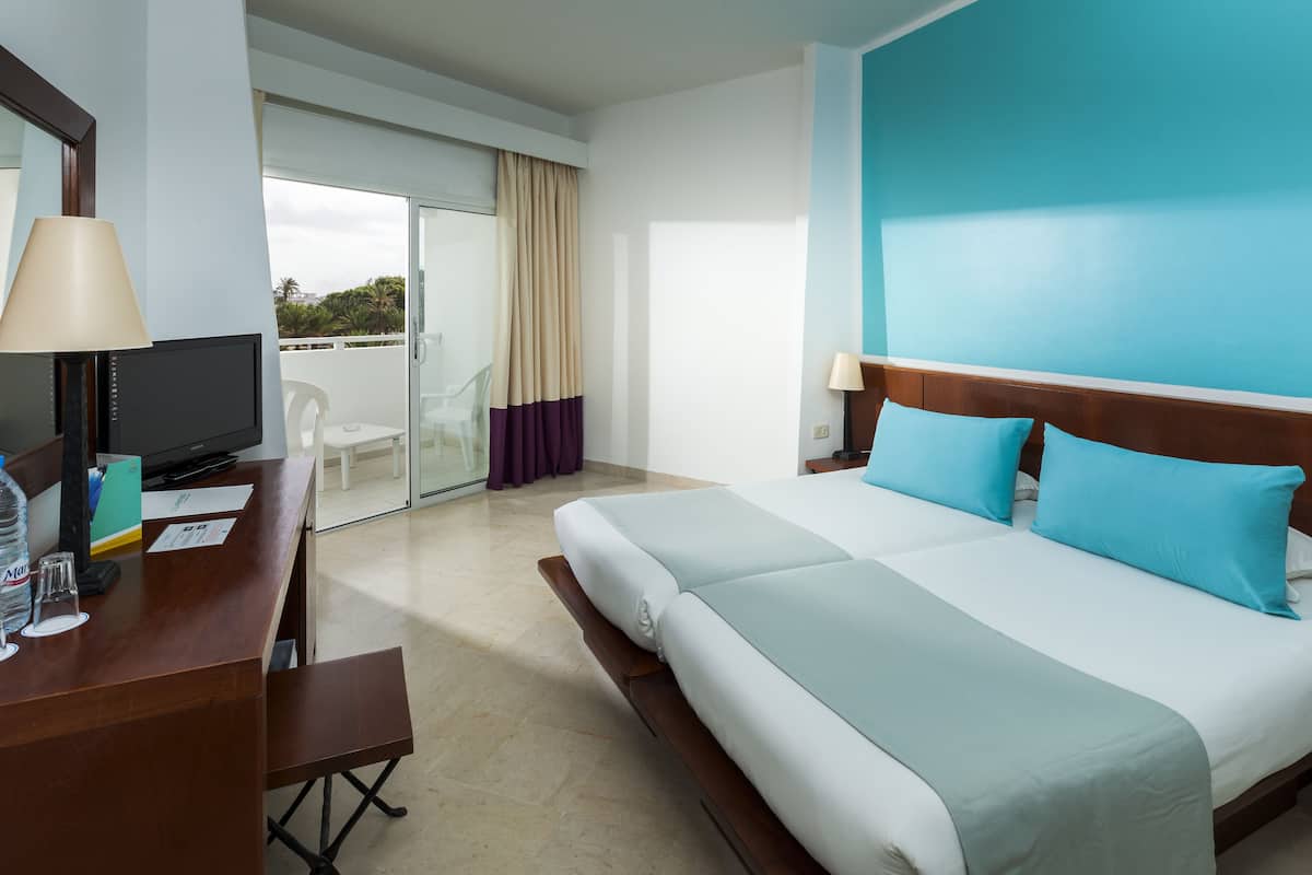 A hotel room with a large bed, a desk with a computer, and a balcony with a view.