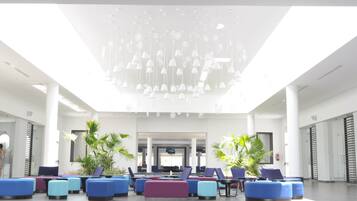A modern lobby with colorful seating, a central chandelier, and palm plants.