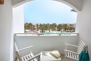 A balcony with white chairs and a table, overlooking a pool area with palm trees and umbrellas. - Palm Beach Club Djerba (Mezraia)