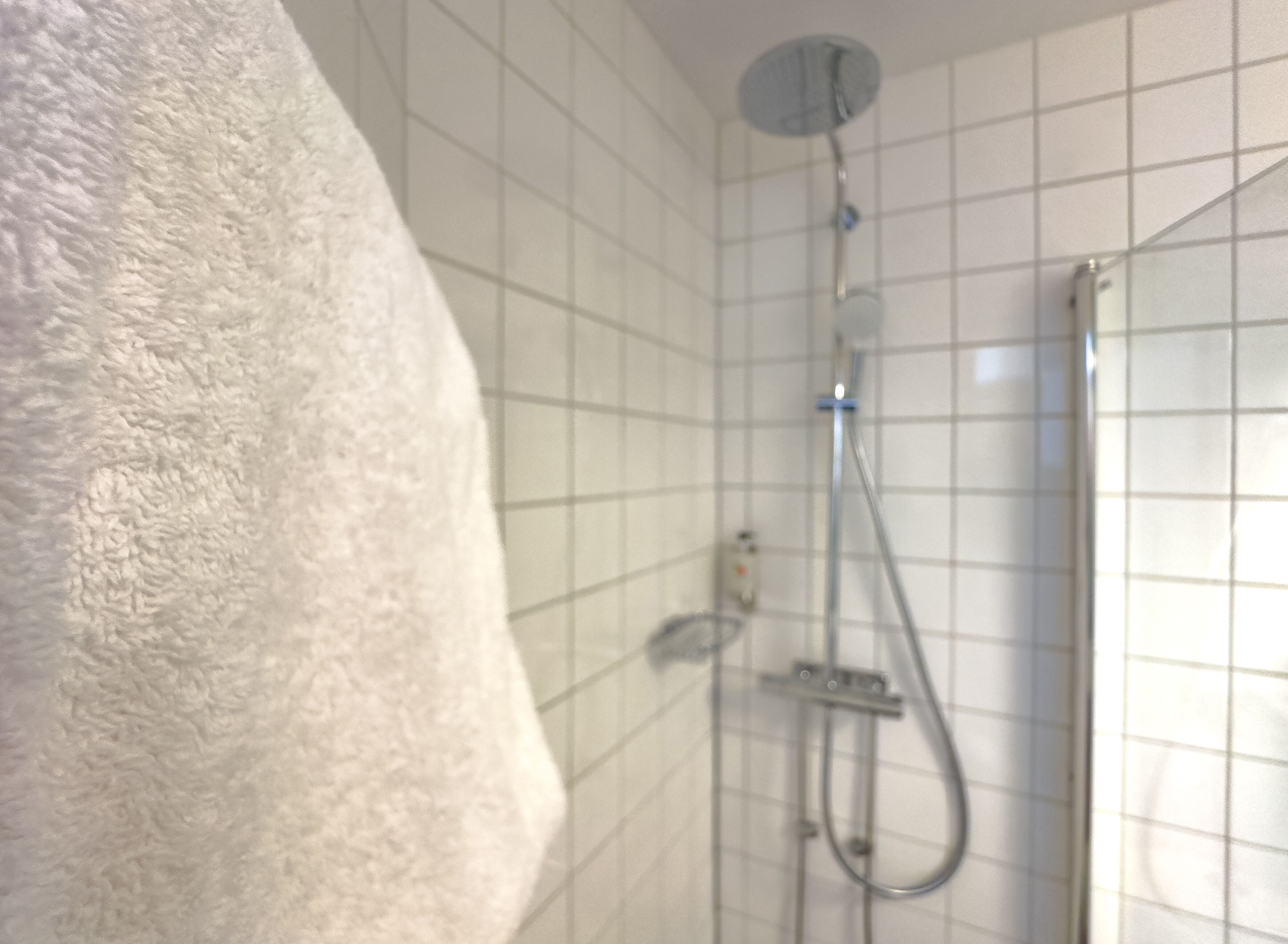 Un baño con ducha, paredes de azulejos y una toalla colgada en la pared.