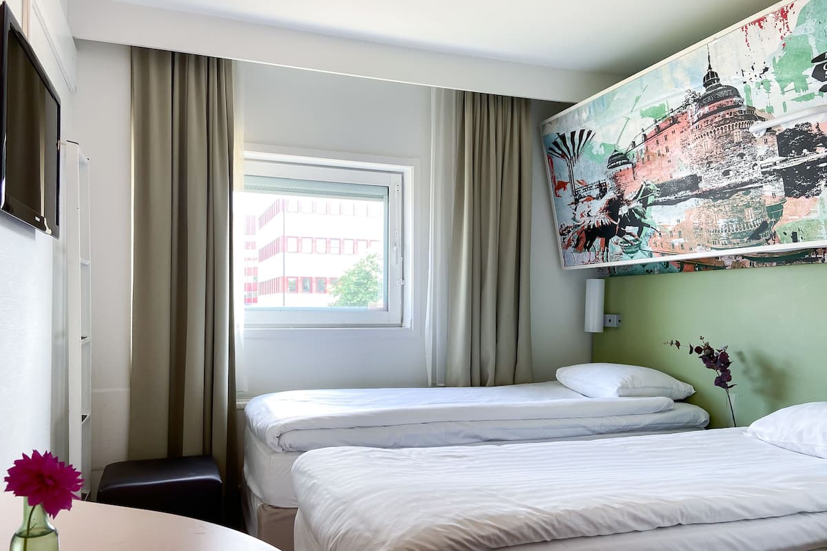 A hotel room with two beds, a window with curtains, a painting on the wall, and a vase with a flower on the table.