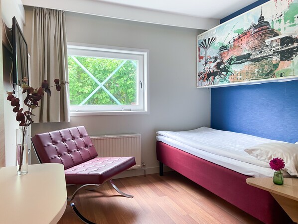 A bedroom with a bed, a chair, a table, a window with curtains, and a painting on the wall.