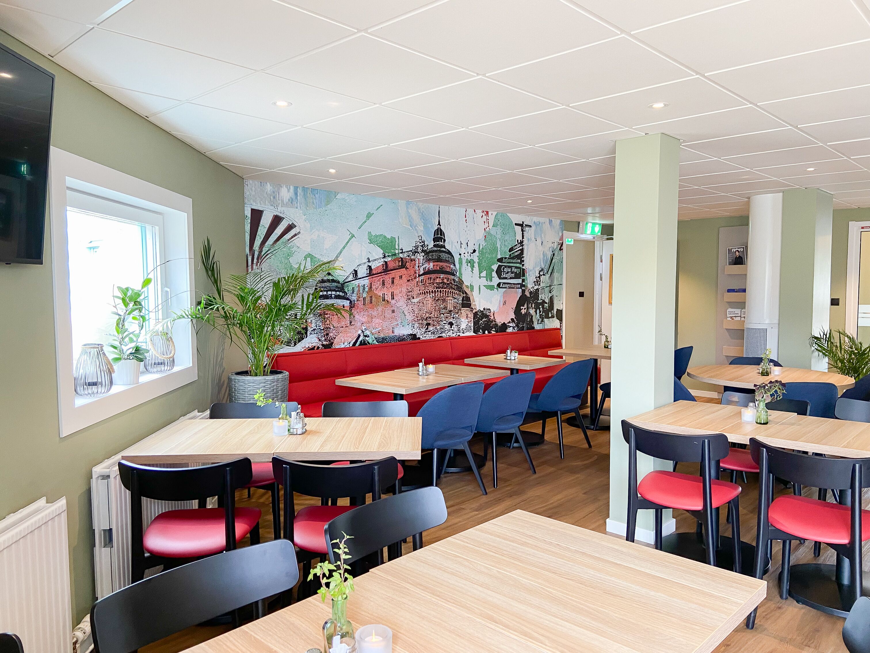 A restaurant with red booths, wooden tables, and blue chairs. There is a mural on the wall depicting a cityscape.