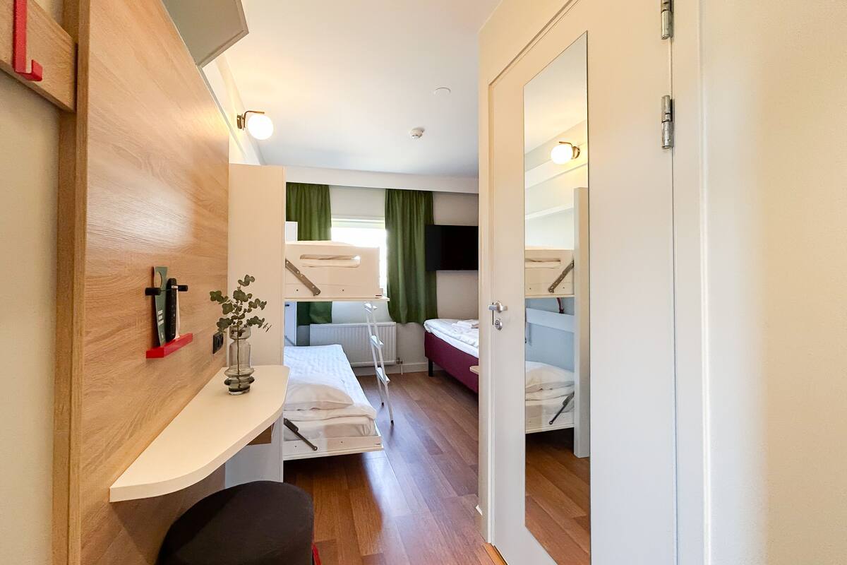 A compact hotel room with a bunk bed, a desk with a chair, a small table, and a mirror.