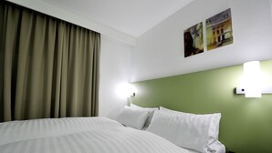 Una habitación de hotel con una cama, cortinas, paredes verdes y dos luces fijadas a la pared.