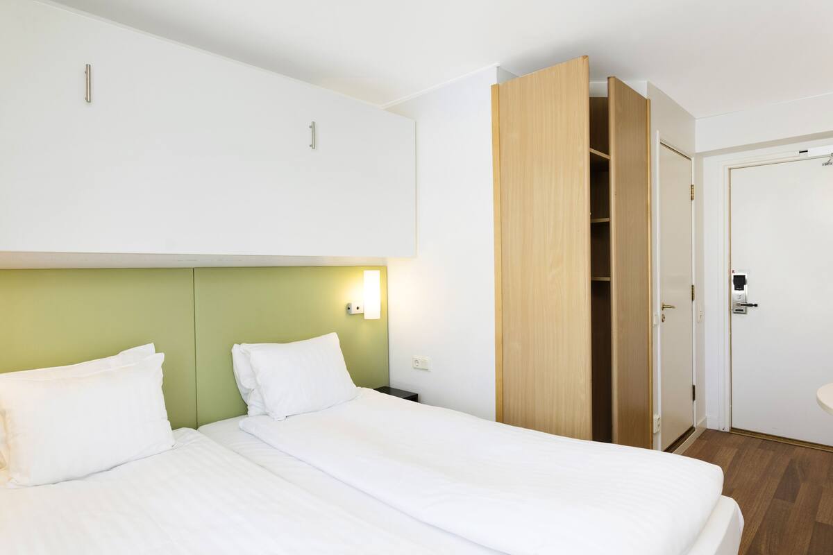 Una habitación de hotel con cama, mesita de noche, luz empotrada en la pared y armario de madera.
