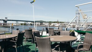 Terraza exterior con mobiliario de mimbre y vista a un puente y al agua.