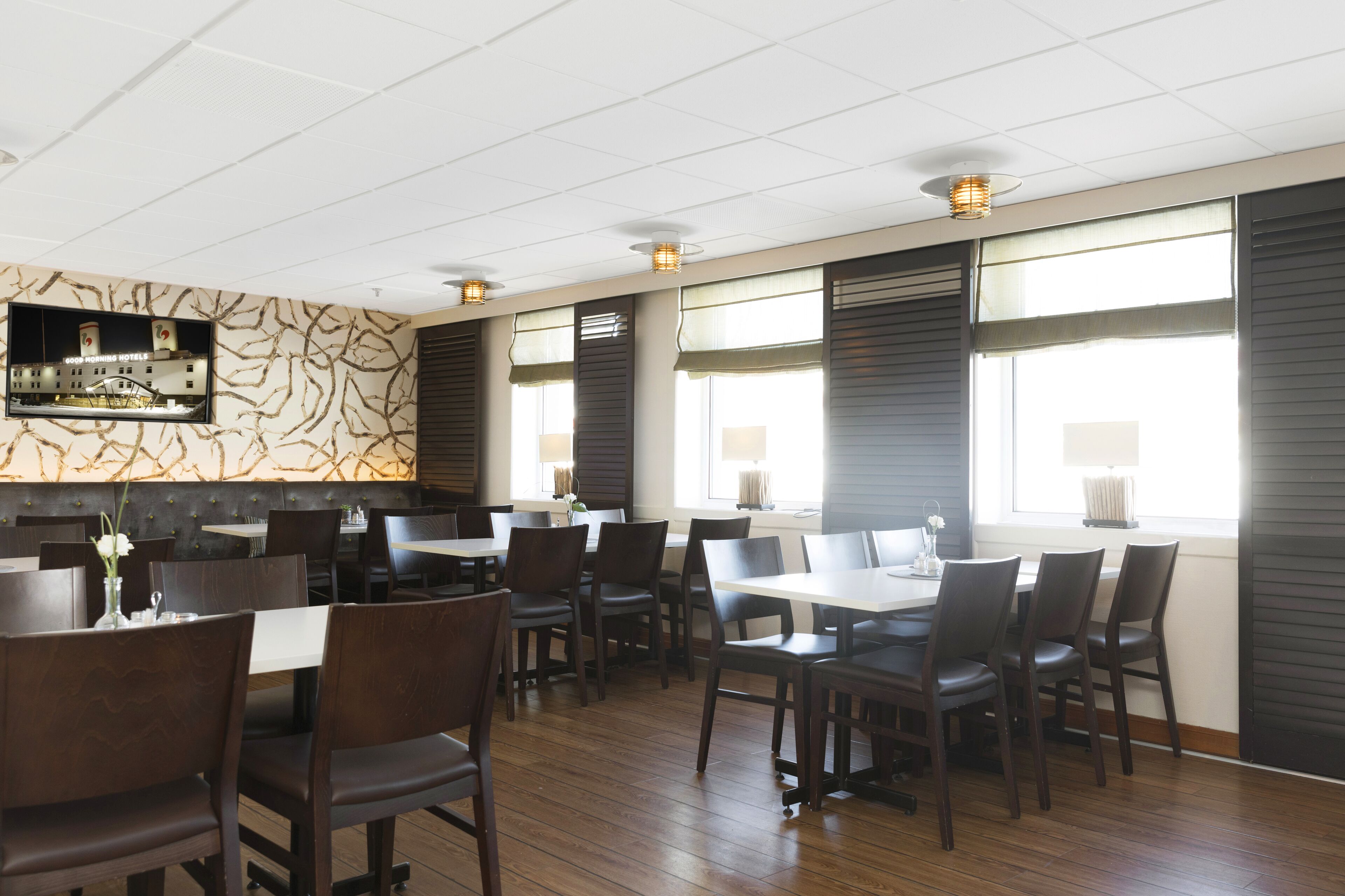 A modern restaurant with wooden flooring, dark-toned chairs, and a patterned wall.