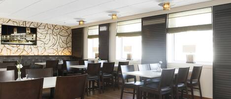 A modern restaurant with wooden flooring, dark-toned chairs, and a patterned wall.