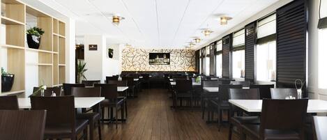 A restaurant with wooden flooring, dark chairs, white tables, and a patterned wall.